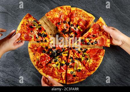 Friends hands taking slices of pizza on dark background. Stock Photo