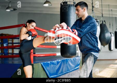 Female boxer kick boxing mitts held by personal trainer at fitness gym Stock Photo