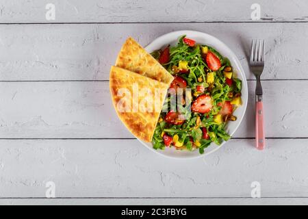 Fresh salad with strawberries, arugula, pineapple and pistachios on white wooden table. Stock Photo