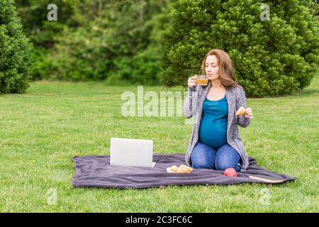 pregnant woman drinking coffee otr tea in the park after working on a computer. Stock Photo