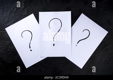 Question marks, written in ink on a piece of standard office paper, shot from the top on black Stock Photo