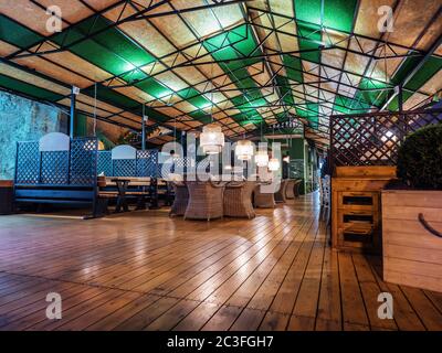 Russia, Sochi 07.22.2019. Evening view of an empty summer cafe with wooden floors, wicker furniture and dim lights Stock Photo