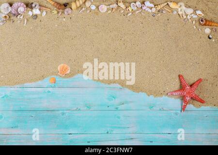 Red starfish with sea shells on sea sand on blue wooden background. Summer or vacation concept. Stock Photo