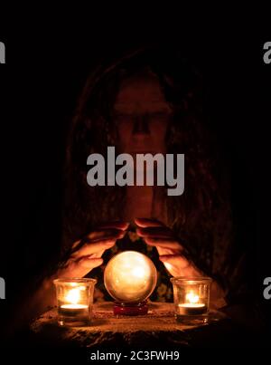 Gypsy woman holding hands over mystical crystal ball with candles Stock Photo