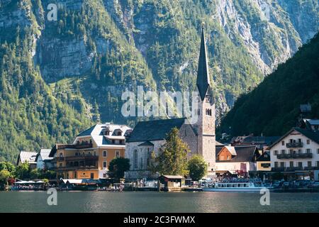 Hallstatt, Austria - June 12 2020: Cityscape of Hallstatt Waterfront with Evangelical Church, Cruise Ship and Seehotel Gruner Baum in the Salzkammergu Stock Photo