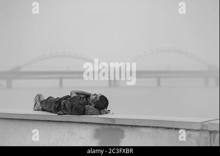 black and white photo a Chinese man sleeping on a parapet on the embankment of the river against the background of the railway bridge in Harbin Stock Photo