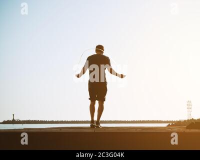Young guy in shorts jumps on a rope on a sunny day on backgraund sky. Artistic effect. Blurred image Stock Photo