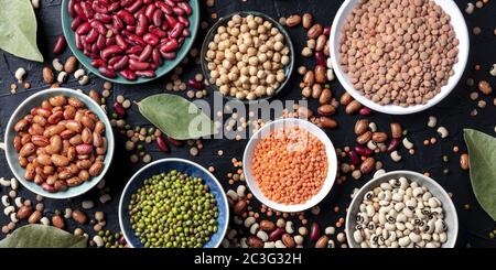 Legumes assortment panorama, overhead shot on a dark background. Lentils, soybeans, chickpeas, red kidney beans, a vatiety of pu Stock Photo