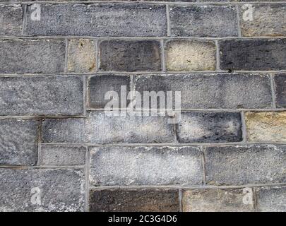 a full frame image of a large old dark stone wall made of large irregular sandstone blocks Stock Photo