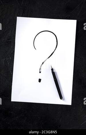 Question mark, written in ink on a piece of standard office paper, shot from above on a dark background Stock Photo