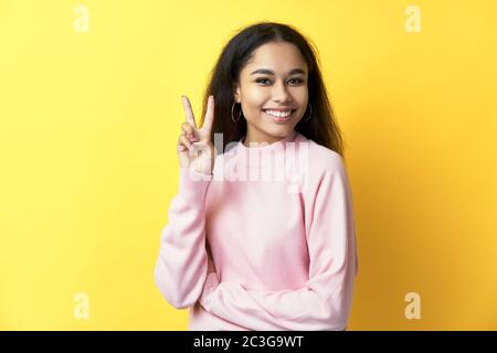 Happy smiling black woman doing victory sign on yellow background. Stock Photo