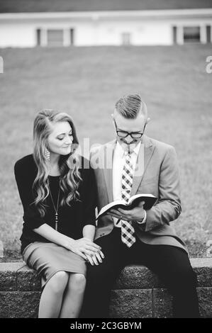 Grayscale of a couple sitting in a garden and lovingly reading a book together Stock Photo
