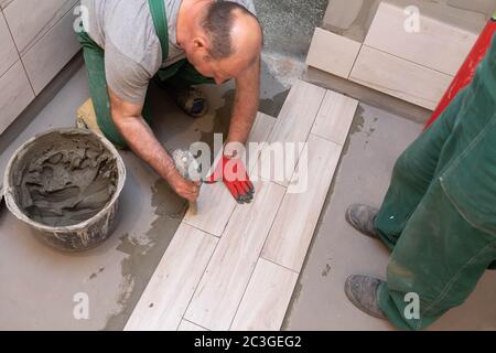 Rubber hammer. An experienced construction worker. Laying terracotta in the bathroom. Work clothes. He knocks with a hammer. Stock Photo
