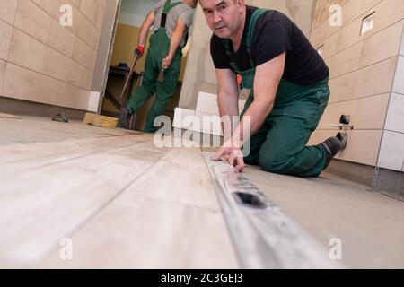 Spirit level - a device for checking the correctness of works performed in relation to the level. A professional construction worker. Kneeling. Stock Photo