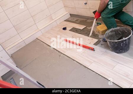 Professional construction worker laying ceramic tiles on the floor in the bathroom room. Stock Photo