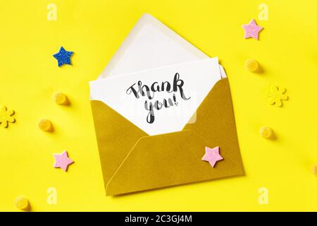 Thank you card in a golden envelope, shot from the top on a yellow background with glitter stars Stock Photo