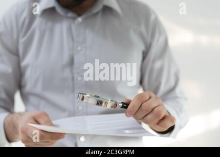 Man in a shirt with long sleeves looking at the papers through the magnifying glass Stock Photo