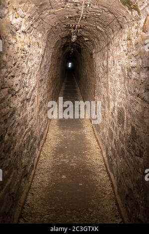 Dark straight cave with light at the end of the tunnel as a metaphor for hope and perseverance Stock Photo