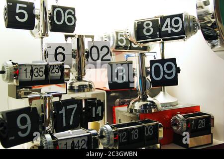 Closeup shot of white and black clocks with different times against a white wall Stock Photo