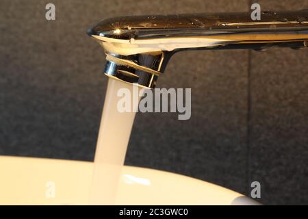 Closeup shot of running water from the metal sink with grey tiles on the background Stock Photo
