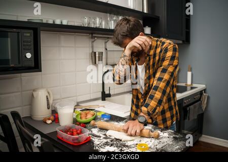 Young man is making cookies in his kitchen. He hates cooking. Stock Photo