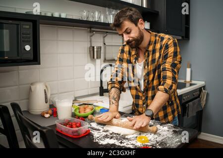 Young man is making cookies in his kitchen. He hates cooking. Stock Photo