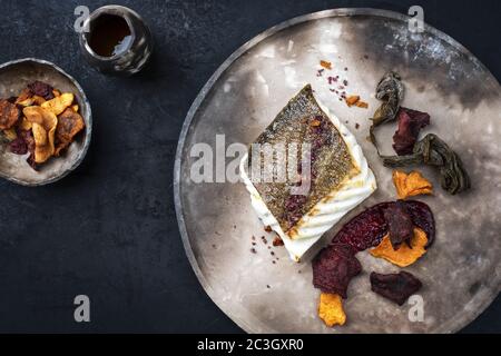 Gourmet fried European skrei cod fish filet with algae and vegetable crisps as top view on a modern design plate Stock Photo