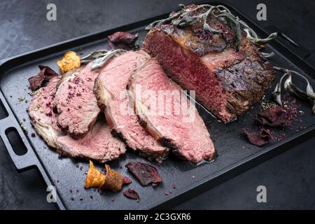 Traditional Commonwealth Sunday roast with sliced cold cuts roast beef with vegetable chips and herbs as closeup on a modern des Stock Photo