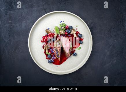 Fried dry aged venison tenderloin fillet medallion steak natural with mushrooms and forest berries as closeup on a modern design Stock Photo