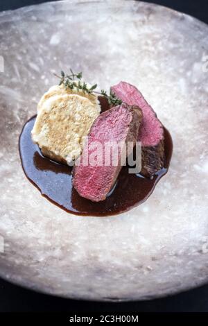 Fried dry aged venison tenderloin fillet medallion steak natural with bread dumpling and spicy gravy sauce as closeup on a moder Stock Photo