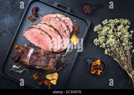 Traditional Commonwealth Sunday roast with sliced cold cuts roast beef with vegetable chips and herbs as top view on a modern de Stock Photo