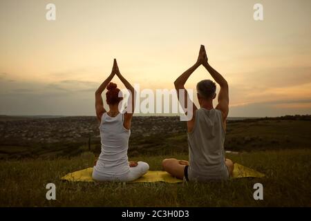 Couple meditating yoga sitting in lotus pose on the nature at dawn. Stock Photo