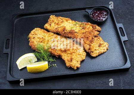 Traditional deep fried Wiener schnitzel from veal topside with cranberry jam and lemon slices offered as closeup on a black mode Stock Photo