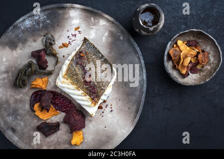 Gourmet fried European skrei cod fish filet with algae and vegetable crisps as top view on a modern design plate Stock Photo