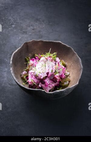 Traditional matie herring with beetroot salad and onion rings offered as closeup in a rustic modern design bowl with copy space Stock Photo