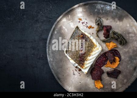 Gourmet fried European skrei cod fish filet with algae and vegetable crisps as top view on a modern design plate with copy space Stock Photo