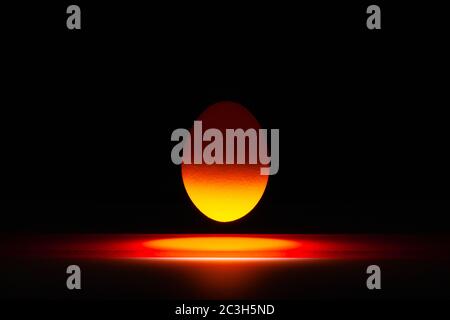 Orange egg levitating over a black glass table in the dark room. Stock Photo