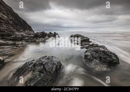 Chapel Porth beach surrounded by rocks and the sea under a cloudy sky in Cornwall, the UK Stock Photo