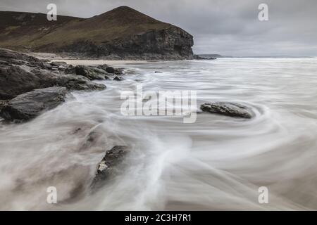 Chapel Porth beach surrounded by rocks and the sea under a cloudy sky in Cornwall, the UK Stock Photo