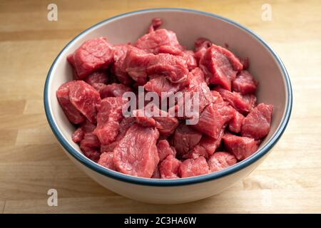 Fresh diced raw beef for goulash or stew in a bowl on a wooden table, cooking at home during coronavirus pandemic, selected focus, narrow depth of fie Stock Photo