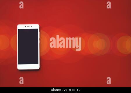 Mockup image of white mobile phone on red background with blank black screen and bokeh Stock Photo