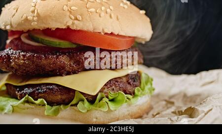 Big appetizing burger with meat cutlet, onion, vegetables, melted cheese, lettuce and mayonnaise sauce on parchment. Isolated hamburger rotates on Stock Photo