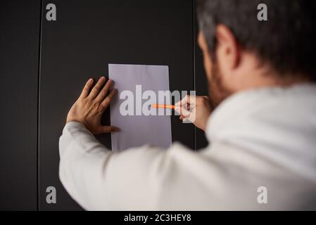 a man writes on a white sheet of paper on a gray background Stock Photo