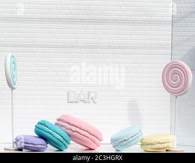 French macarons or macaroons with lollipops and copyspace on a white brick wall with sign saying Bar Stock Photo