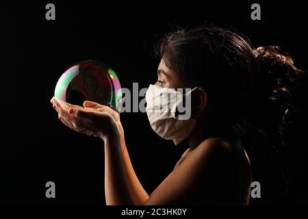 Midshot of a girl catching soap bubble  by wearing mask resemble a kid hopping for COVID free new world. Stock Photo