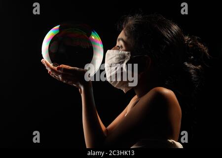 Midshot of a girl catching soap bubble  by wearing mask resemble a kid hopping for COVID free new world. Stock Photo