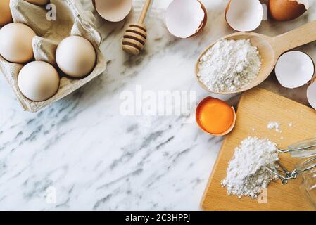 Baking utensils and baking ingredients with eggs, wheat flour, egg yolks for pastry. Cake, pasta or dough recipe ingredients. Top view on table Stock Photo