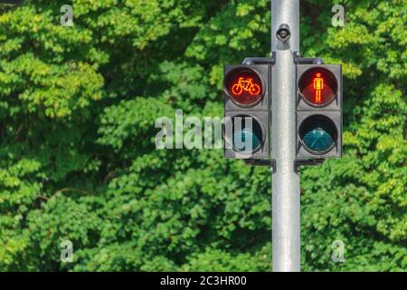 Red traffic lights for pedestrians and cyclists on green trees foliage. Safety on roads concept. Life insurance. Stock Photo