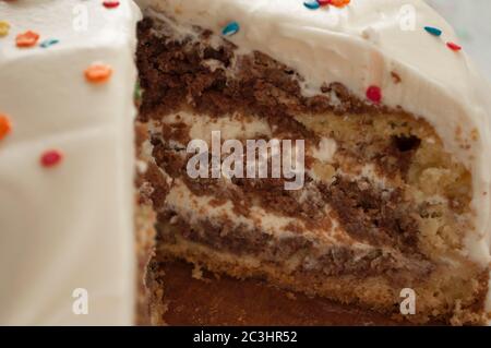 Chocolate sponge cake with cream close up decorated with multicolored topping. Whole cake with a cut piece, macro photography Stock Photo