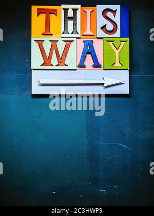 Closeup shot of colourful THIS WAY and arrow pointing right on the blue background Stock Photo